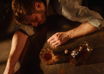 a man sleeps on a table with a bottle of whiskey