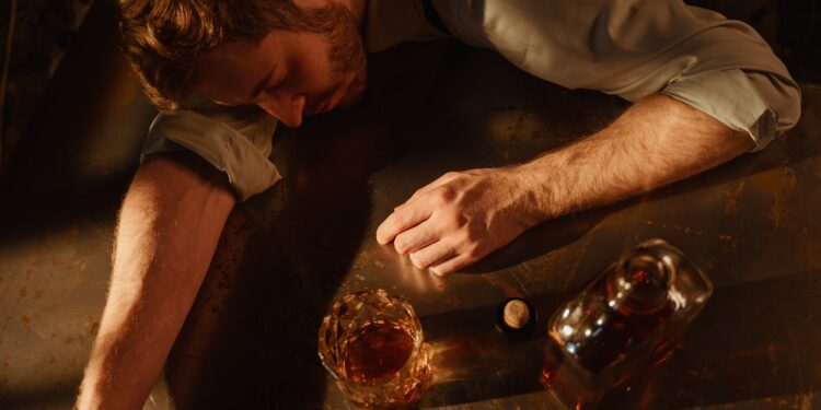 a man sleeps on a table with a bottle of whiskey
