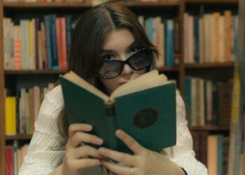 woman with sunglasses reading book in library