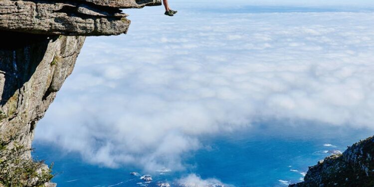 person sitting on mountain cliff: The poem opens with the personification of nature, framing climate change as a message—an alarm that humanity must heed. This sets the tone: the Earth is in crisis, and it is calling out for rescue.